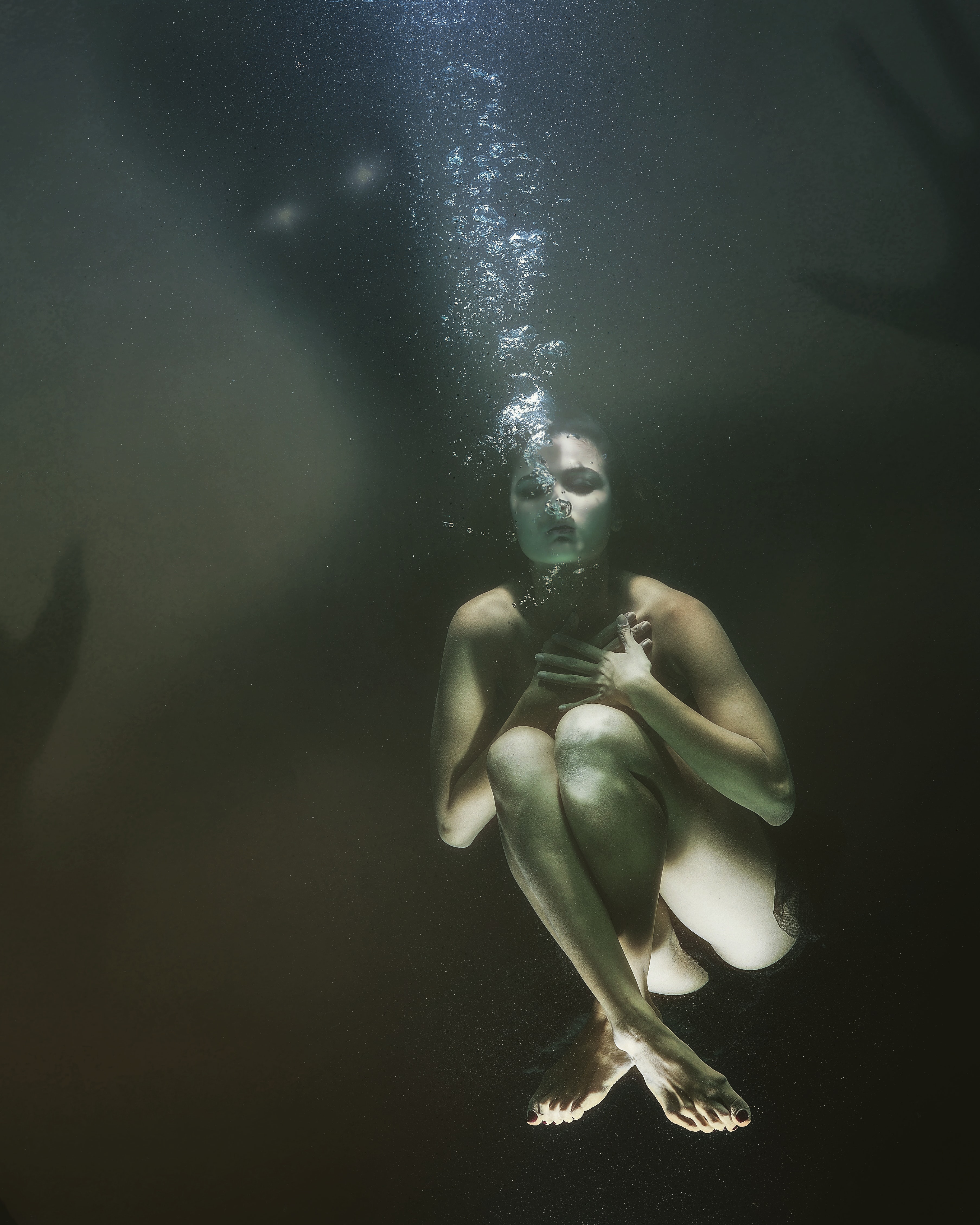 A woman underwater, drowning, with a dark shadowy figure around her