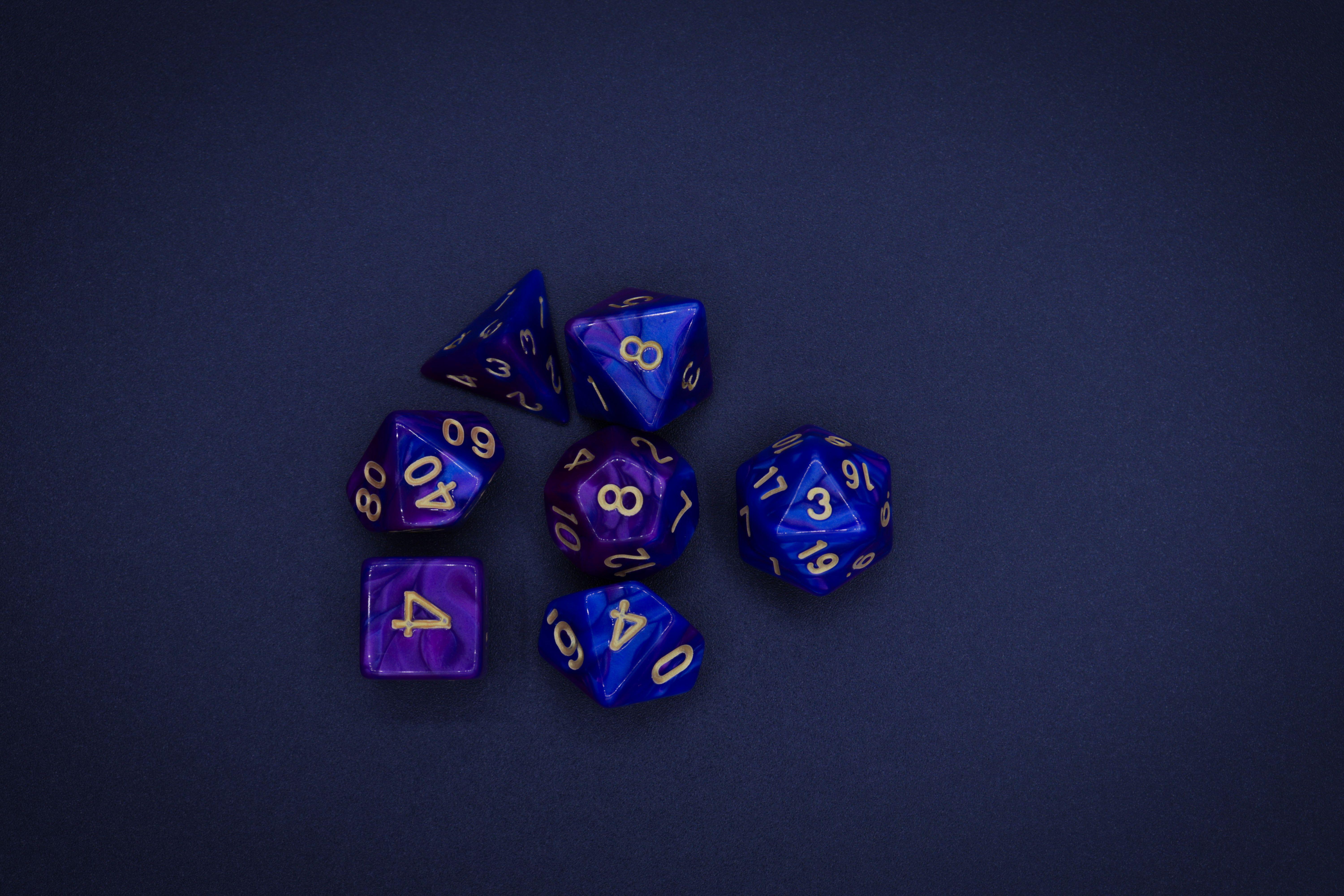 A set of starry indigo and purple polyhedral dice against a dark blue background