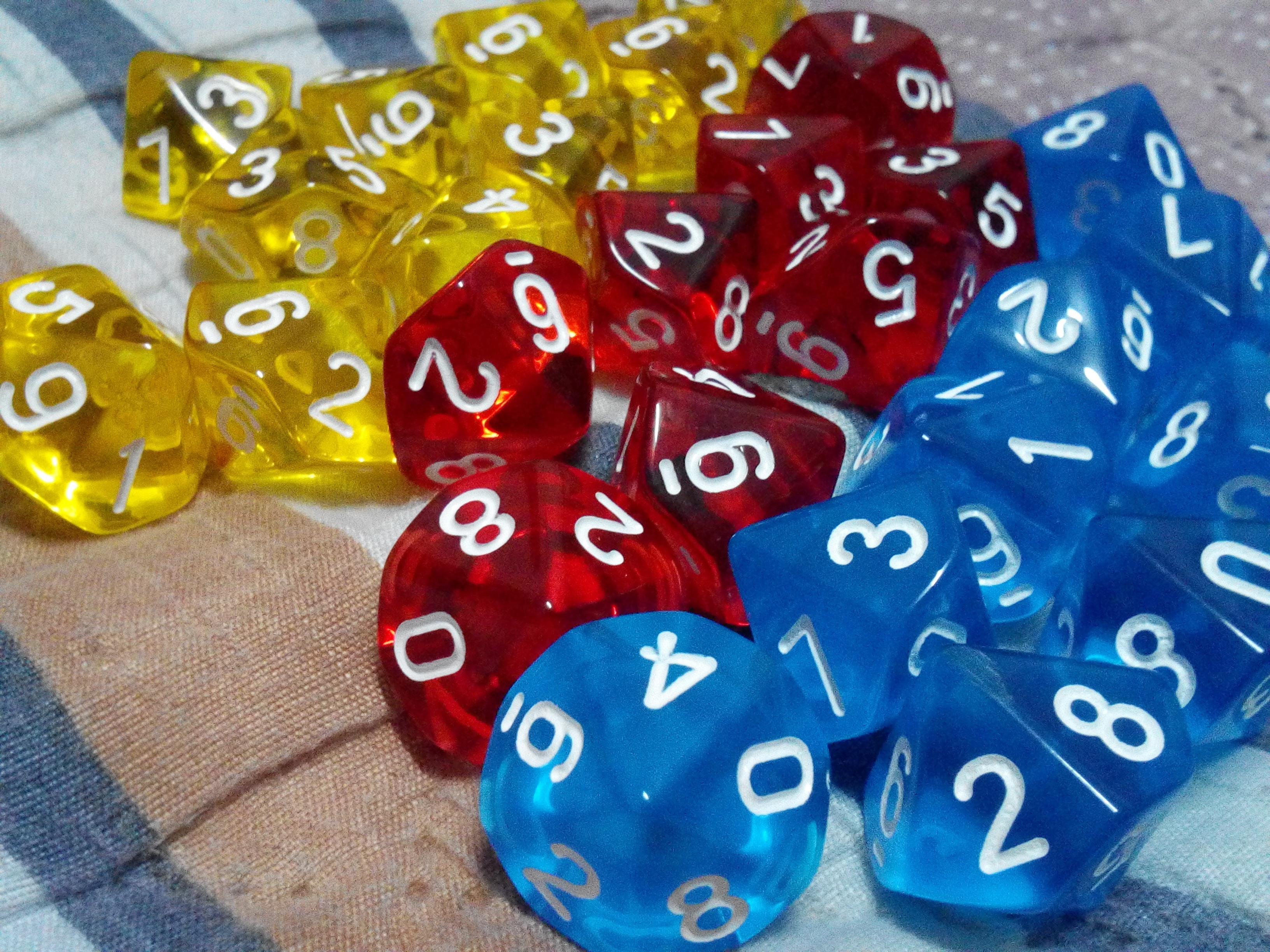 Three sets of translucent polyhedral dice in yellow, red, and blue