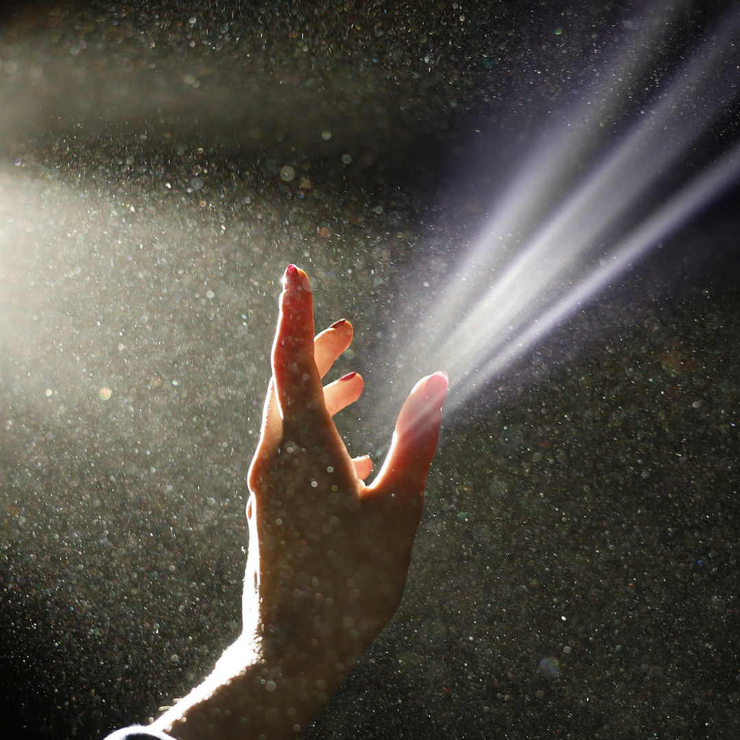 A hand illuminated by a sunbeam in a dark room, projecting a glowing ray of light from its palm