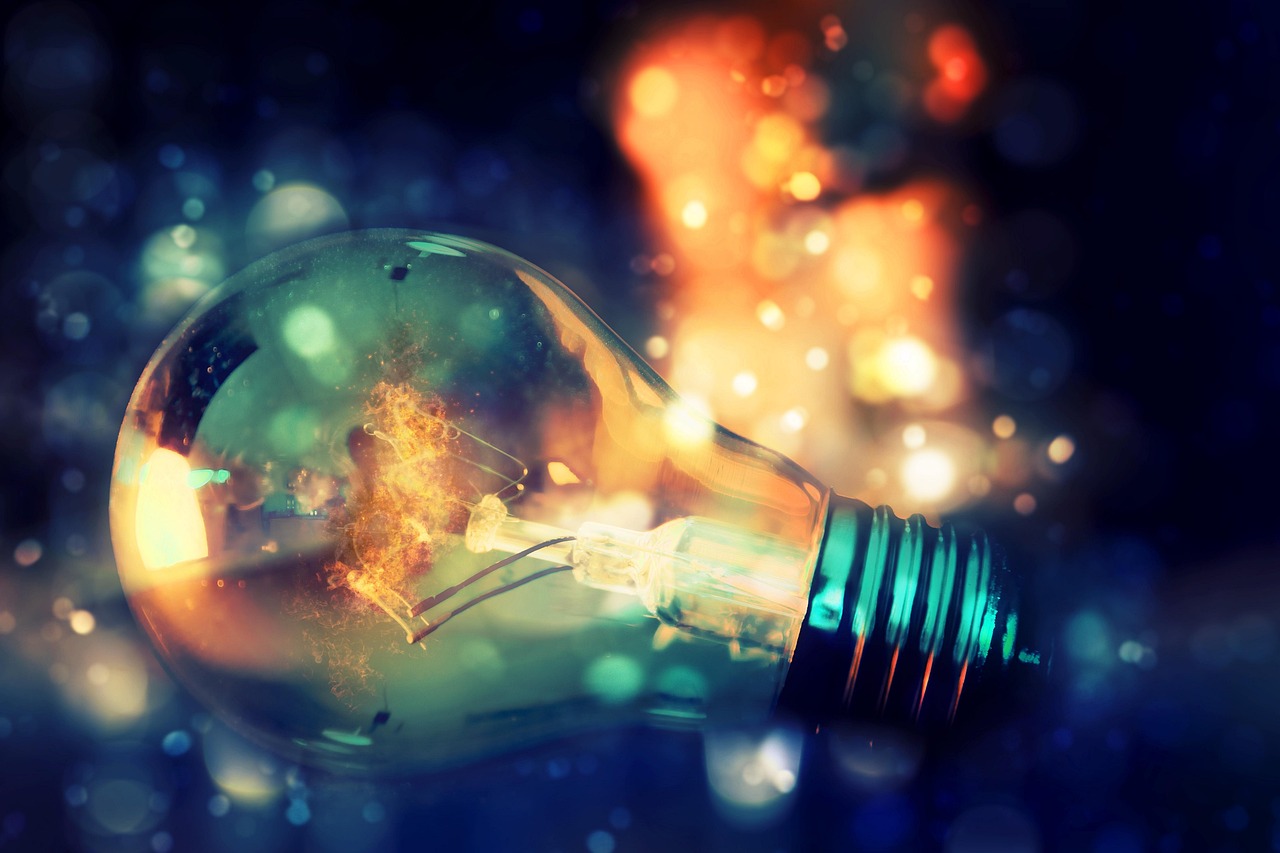 A light bulb with fire arcing between its filaments against a bokeh blue and orange background
