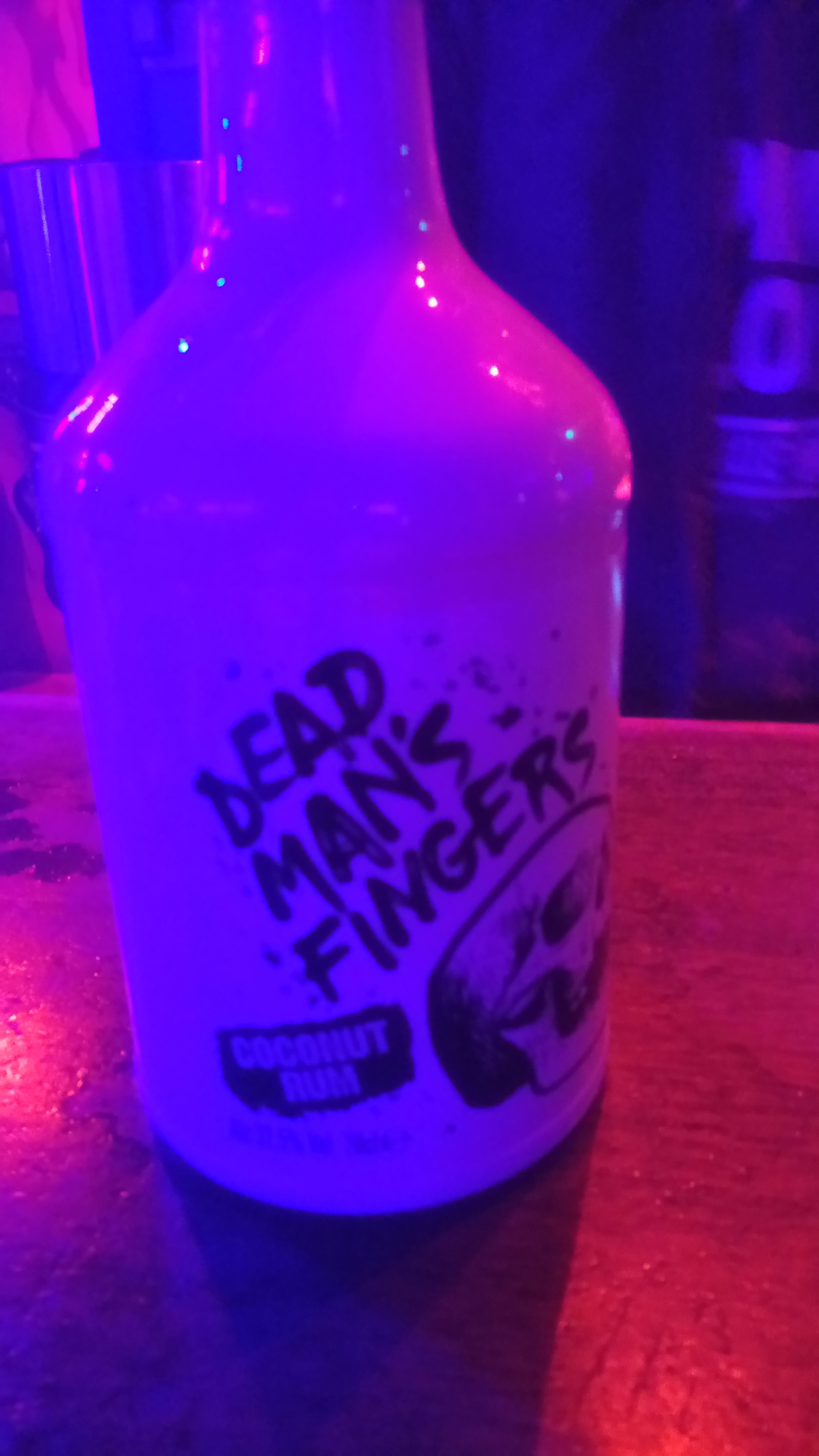 A white bottle of coconut rum in a purple neon bar, with a skull design and the name 