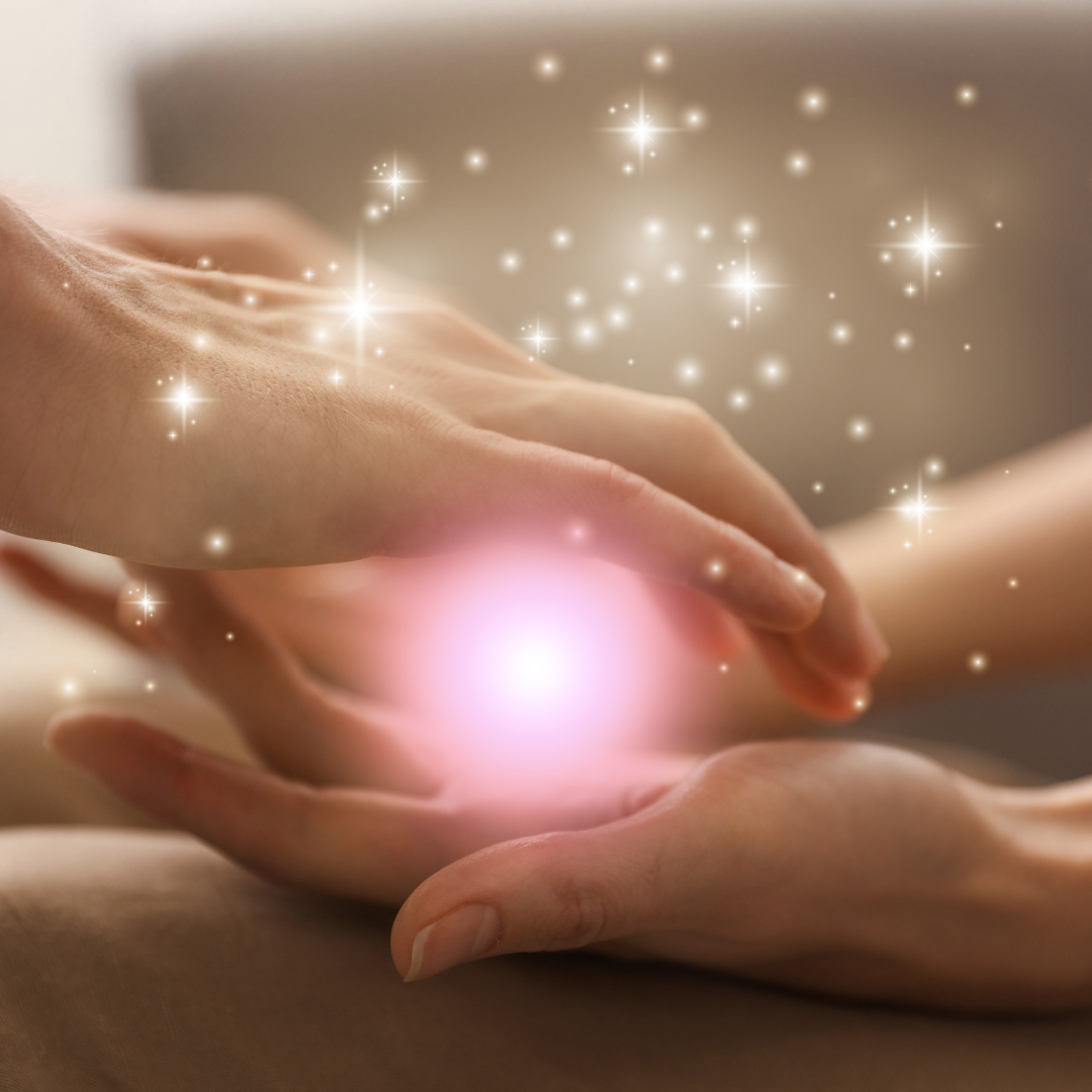Two sets of hands, with the one raised over top projecting a glowing pink light into the other, surrounded by sparkles