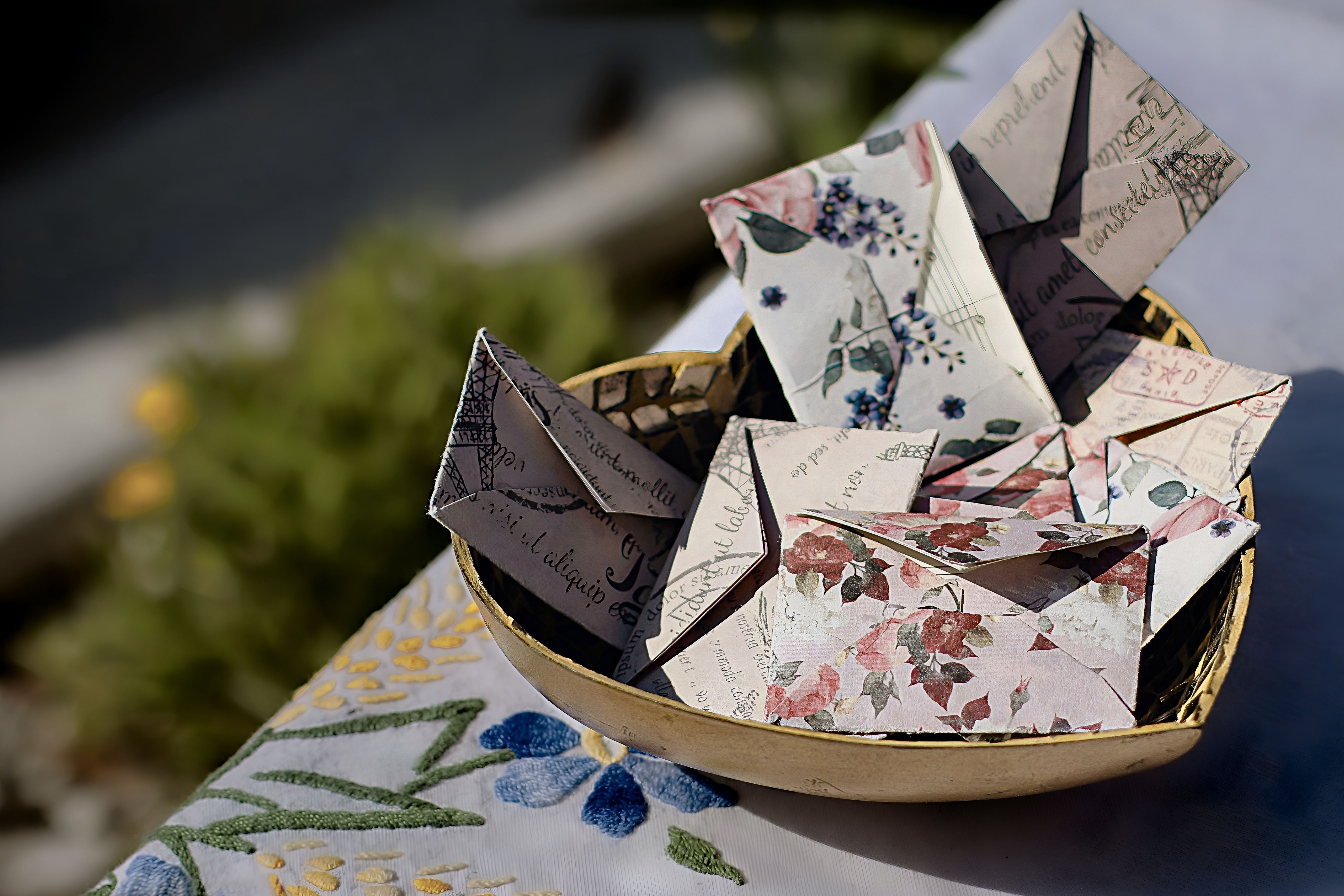 Origami folded letters in floral vintage prints, on the edge of a picnic table with a decorative tablecloth