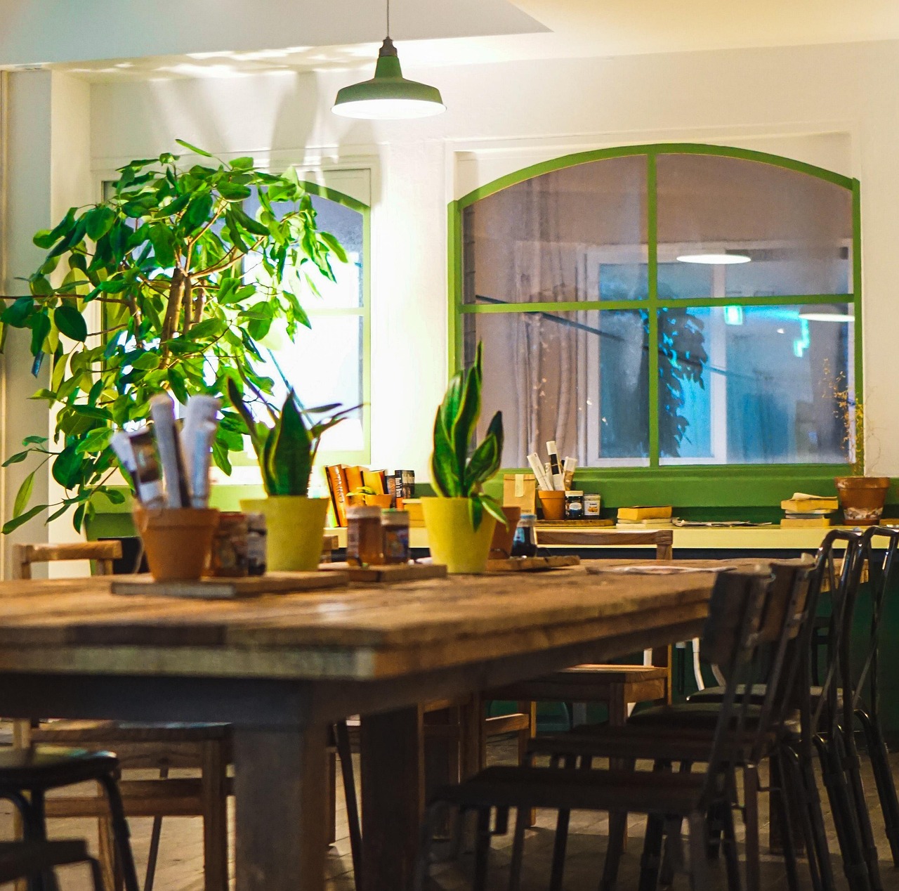 coffee-shop-5610182_1280.jpg A brightly lit coffee shop interior with arched, green-framed windows and whimsical plants, with books to read visible on a back shelf